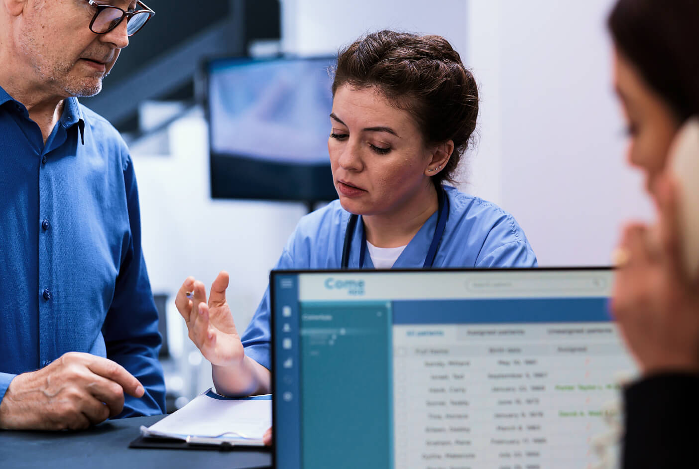 Nurse at desk engaged with mature man, describing what she sees on clipboard.