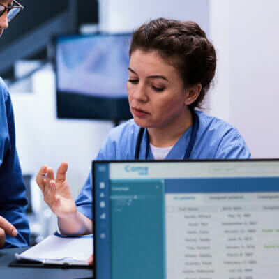 Nurse at desk engaged with mature man, describing what she sees on clipboard.