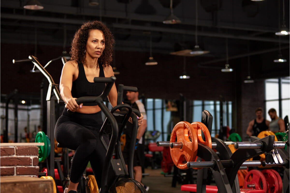 A fitness gym setting with woman riding on exercise bike.