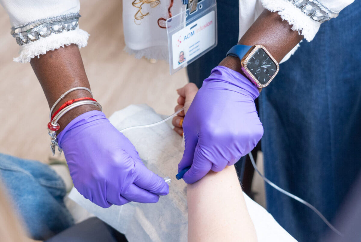 A nurse wearing purple latex gloves starts a patient's infusion